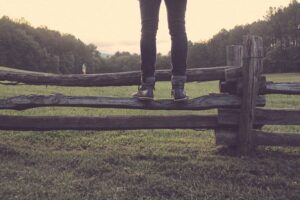 A person standing on a fence in a field.
