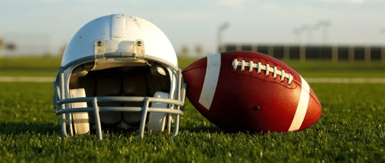 A white football helmet and a brown football on grass with a blurred background during daylight.