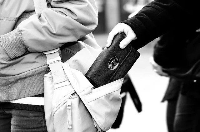 A hand stealing a wallet from a bag.