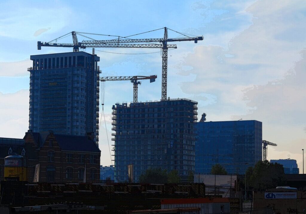 A group of construction cranes in front of a skyscraper.