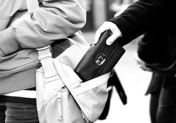 A hand stealing a wallet from a bag.