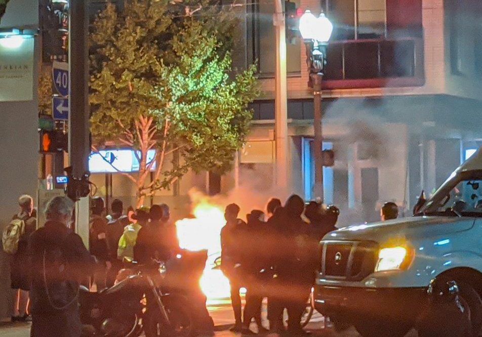 A burning car at night with people standing around it.