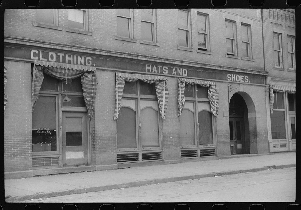 Black and white storefront with clothing, hats, and shoes.